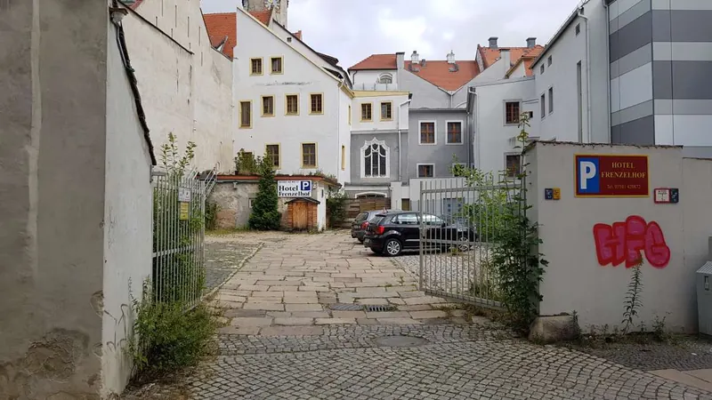 Il cortile oggi: un passaggio lastricato tra edifici posteriori chiari e restaurati, tetti sullo sfondo.