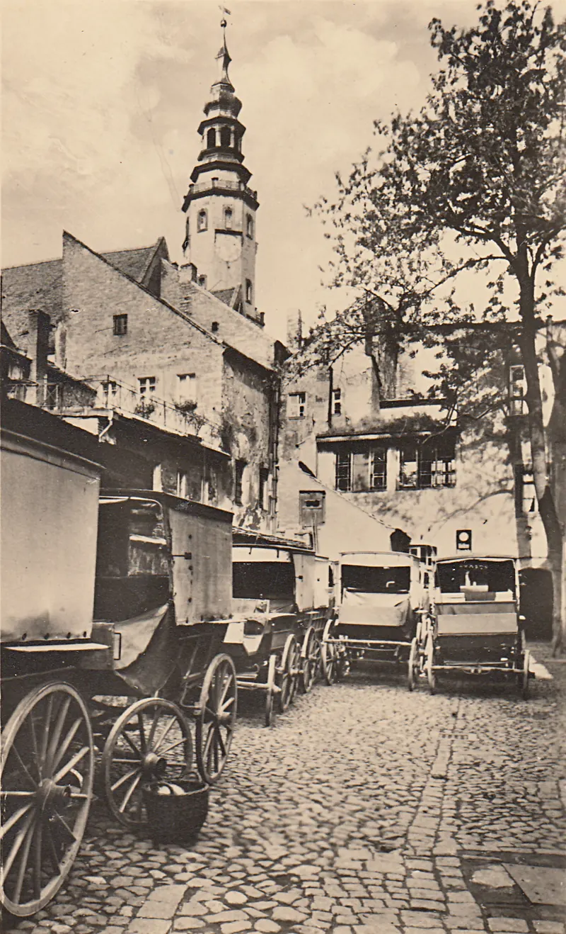 Cartolina del 1920 circa: il cortile come angolo pittoresco con graticci, carri e la torre del municipio sullo sfondo.