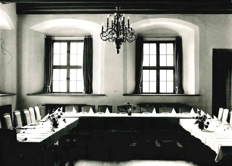 Foto in bianco e nero del 1976: il salone con lampadario e una lunga tavola, le travi sul soffitto.