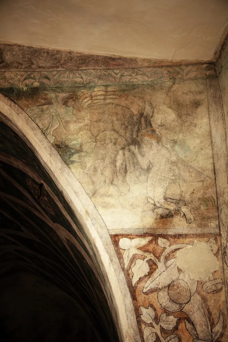 Pittura murale molto danneggiata nel pennacchio della volta: resti di una figura inginocchiata davanti a una roccia.