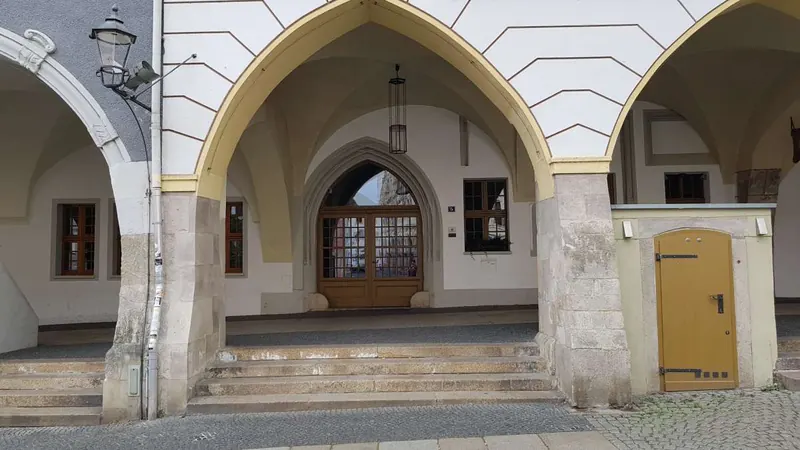Vista sotto i portici sul portale ad arco acuto con porta in legno e gradini davanti.